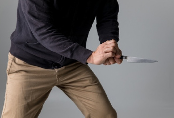 黒い服の男が攻撃的に刃物を握りしめている様子